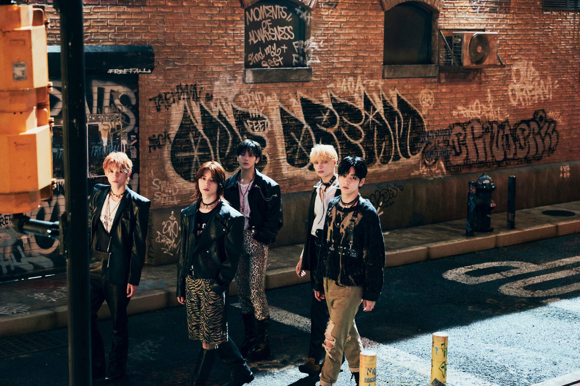 A picture of all five members of the Kpop group TXT (Tomorrow By Together) walking down a graffiti'd alleyway.
